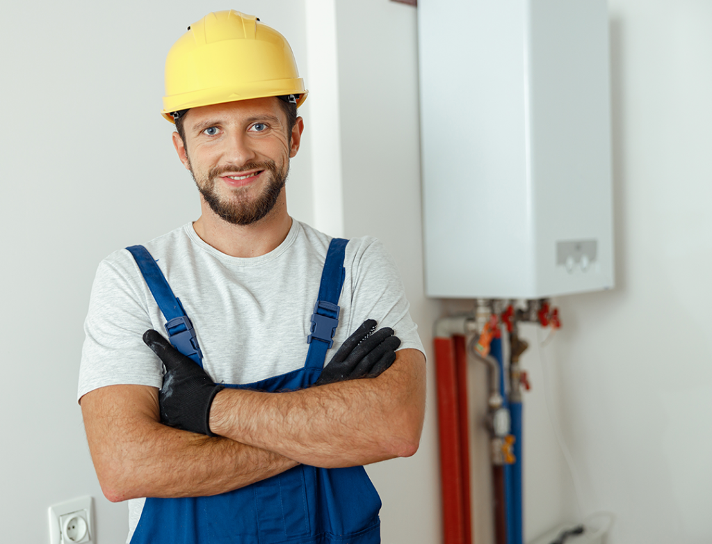 Smiling heating engineer in a hard hat beside a boiler